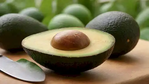Aguacate fresco, madura pero no sobreripe, colocado en una tabla de corte de madera, rodeado de hojas verdes exuberantes, con un pequeño cuchillo y placa en el fondo, fuente de luz cálida, tonos terrenales