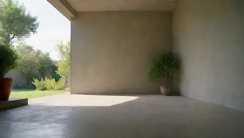 Un hogar tranquilo y sereno interior con un esbozo débil de las paredes de la fundación, grietas en hormigón y sombras sutiles, rodeado de vegetación exuberante y un cielo soleado, transmitiendo un sentido de reparación y renovación