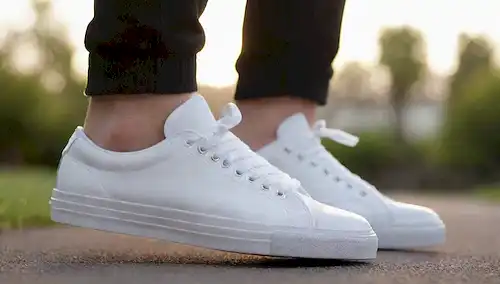 zapatillas blancas limpias con un toque de brillo en las tapas de dedo, cordones ligeramente escruzados, pliegues suaves en el material superior, y un reflejo débil de las suelas, con un fondo suave y borroso con sombras sutiles