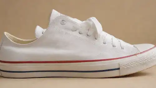 Zapatos blancos limpios con cordones removidos, en un fondo de color claro, con sombras sutiles que resaltan sus contornos, y posiblemente algunos pequeños pliegues o pliegues para sugerir desgaste, pero en general aparecen limpiados de forma fresca