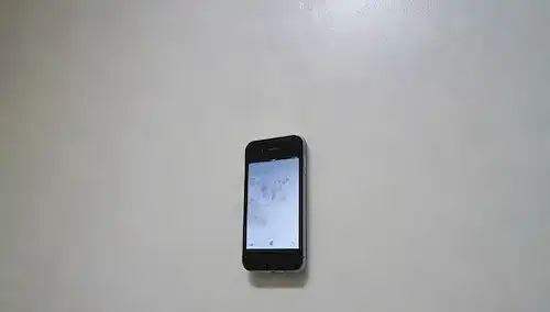 Una pared húmeda con manchas de agua, un teléfono inteligente parcialmente sumergido en agua, un pequeño ventilador o deshumidificador cerca, un fondo blanco, un efecto gradiente sutil para representar la humedad, un sentido general de humedad y humedad, un diseño limpio y minimalista, un enfoque en la pared y el entorno circundante