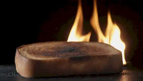 Un brindis quemado con bordes ennegrecidos, rodeado de un resplandor o humo débil, en un fondo oscuro para enfatizar su apariencia peligrosa, con textura crujiente y frágil, con posibles grietas y grietas, transportando peligro y toxicidad