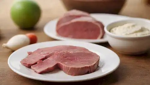 Un plato con un corte de carne roja y un corte de carne blanca, lado a lado, en una mesa de madera rústica, con un fondo borroso de una granja o una carnicería, en colores cálidos como marrón y beige, con luz natural de la derecha, destacando la frescura de los ingredientes