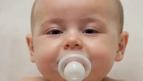 Una cara de bebés con un chupete en su boca, rodeado de un fondo blanco suave, con una suave sonrisa, ojos cerrados y una expresión facial relajada, con una sombra sutil o un punto culminante para transmitir profundidad