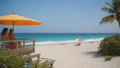 Una escena de playa serena con unas cuantas personas relajándose bajo sombrillas coloridas