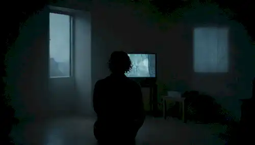 Una persona sentada sola en una habitación oscura, rodeada de espacio vacío, con una fuente de luz débil, y una pantalla de TV o portátil brillando, transmitiendo sentimientos de soledad, aislamiento y desconexión del mundo exterior