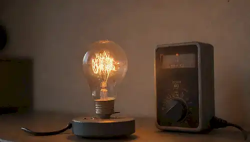 Una bombilla brillante con un filamento desgastado, un medidor eléctrico anticuado y un medidor inteligente en el fondo, rodeado de sutiles indicios de flujo de energía y eficiencia, como alambres brillantes, chispas o rayos, con un enfoque suave para transmitir un sentido del cambio y la innovación