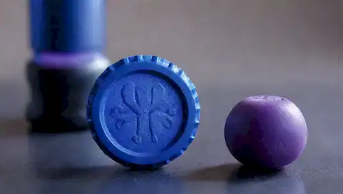 Un disparo de cerca de una tapa de botella con una estructura molecular o un símbolo de riesgo biológico, junto a un par de muñecos y un cerebro rodeado por un sutil gradiente de tonos azules y púrpuras