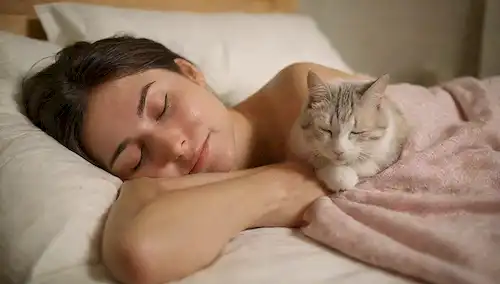 Una persona acurrucada en una cama con un gato durmiendo o acostado a través de su cuerpo