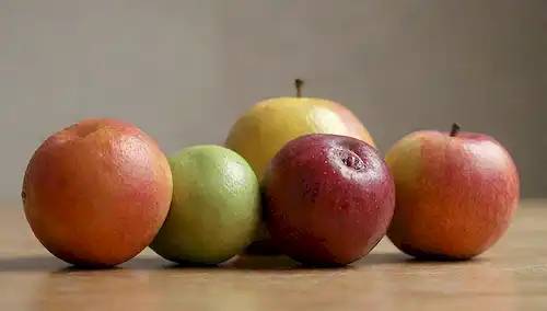 3-5 frutos maduros con formas, colores y texturas distintas, colocados sobre una superficie de madera, rodeados de sombras sutiles, contra un fondo gris suave o beige, que transmite una sensación de naturalidad y sencillez, con un enfoque suave en las diferencias entre cada fruta