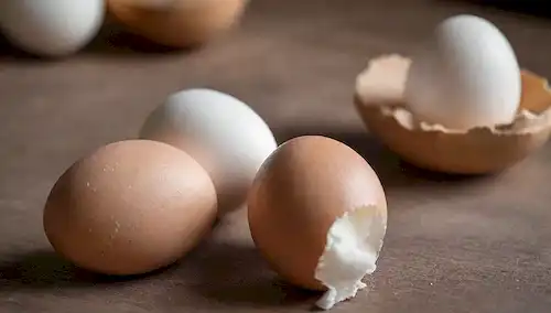 2 huevos con cáscaras marrones y blancas lado a lado en una mesa rústica, fuente de luz natural de arriba, superficie de madera ligeramente desgastada, enfoque suave para resaltar la textura, sombras sutiles para transmitir profundidad