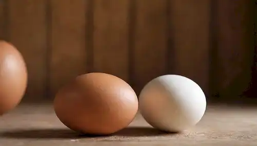 2 huevos marrones y 2 huevos blancos sobre una mesa, cada uno con su propia textura y patrón únicos, sobre un fondo cálido de madera, iluminación suave, utilería mínima, tono rústico, colores naturales