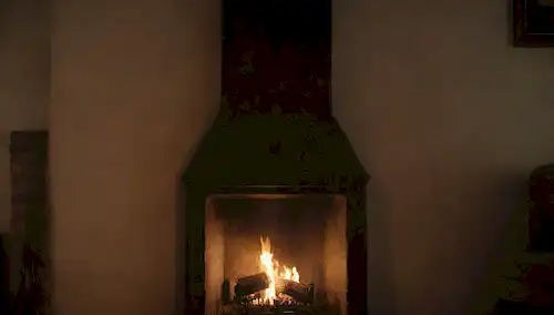 Una persona, aire oscuro y novato, humo que sale de una chimenea, un resplandor cálido, un ambiente acogedor, preocupación en su expresión, un esbozo débil de una chimenea o corazón en el fondo, sombras en la pared