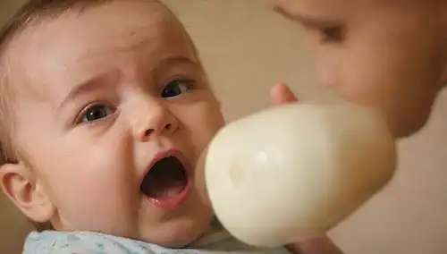 Un bebé feliz y curioso con una botella siendo cuidadosamente quitada por un padre o cuidador cariñoso; un disparo de cerca de los bebés cara reaccionando al cambio; un ambiente cálido y acogedor enfermero; iluminación suave y natural; un toque de juguetes u otros objetos estimulantes en el fondo