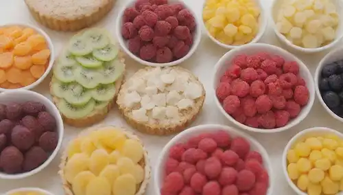 Un arreglo de dulces de colores brillantes y perfectamente arreglados, tales como caramelos, productos horneados y aperitivos de frutas, con unas pocas sutiles indicios de elementos inspirados en la naturaleza como hojas o flores, situados en un fondo blanco limpio con un tono cálido, que transmite el sentido de bondad natural y solidez, posiblemente con algunas sombras suaves o momentos destacados para dar profundidad y dimensión