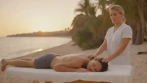 Una escena de playa con una mesa de masajes sobre arena, terapeutas manos masajeando hombros clientes, olas chocando suavemente en el fondo, sol sentado detrás de palmeras, expresión facial relajada, ambiente sereno, ambiente tranquilo