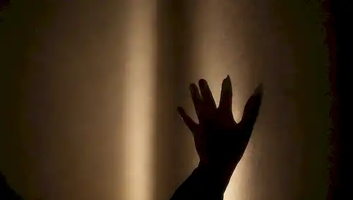 Una persona en un cuarto oscuro con luces brillantes, manos temblando en una pared, rodeada de sombras lencerias, con un ligero indicio de desesperación y ansiedad, transmitiendo sentido de estar atrapada, abrumada y desorientada