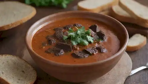 Un cuenco cálido y rústico lleno de sopa chichurro chunky, rematado con una generosa ayuda de morcilla desmoronada, adornada con riegos cilantro frescos y rodajas de pan crujiente junto con