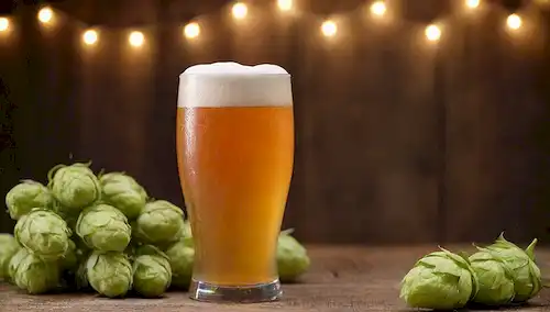 Cerveza de color amarillo nublado con cabeza blanca gruesa, cono de aro o ramillete de aro en primer plano, fondo rústico de madera, elementos industriales vintage, velas o luces de hadas para el ambiente