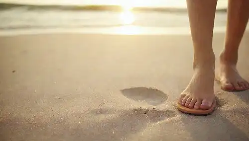 Un pie de personas con chanclas en, escena de playa de verano en el fondo, arena y agua salpicando, cálida luz del sol echando un resplandor, suave brisa soplando, ambiente relajado