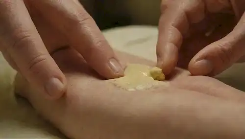 Una mano suavemente aplicando una pasta verde-amarillo en una articulación artrítica, con una sutil sonrisa que transmite alivio, rodeado por calmante luz cálida y colores calmantes, mostrando la facilidad de aplicación, al tiempo que destaca el área afectada en un enfoque suave
