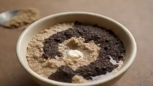 Un cuenco lleno de aceite usado reciclado mezclado con ingredientes naturales, como azúcar, café o avena; unas gotas de aceites esenciales en la parte superior; una cuchara y un cepillo en estrecha proximidad; un fondo con tonos terrenales; un toque de brillo de la mezcla; enfoque suave para transmitir una sensación de fabricación casera y orgánica; una luz cálida y acogedor