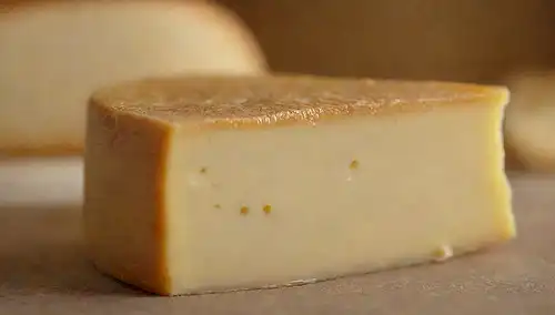 Queso suave, superficie dorada, corteza blanca, pequeñas grietas, pliegues delicados, bordes crumbly, centro cremoso, textura ligeramente translúcida, fondo de enfoque suave, iluminación cálida