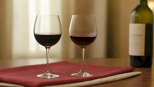 3 vasos sobre un mantel de madera, botella de vino en fondo, foco suave, iluminación cálida, reflejos de borde dorado, textura sutil, vinos tintos y blancos